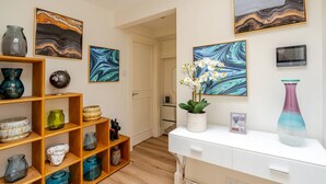 Een hal met een witte console tafel, planken met decoratieve objecten, en abstracte schilderijen aan de muur.
