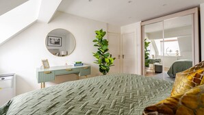 Een slaapkamer met een groot bed, een bureau, een spiegel en een plant.