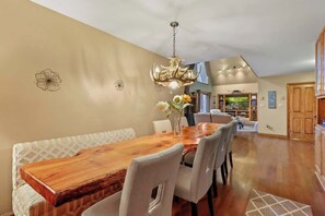 A dining area with a wooden table, white upholstered chairs, a chandelier, and a vase with flowers. - A-Frame Of Mind: Mountain Escape (Beech Mountain)