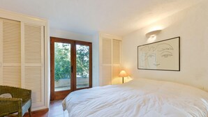 Um quarto com uma cama, uma cadeira, uma porta que dá para uma varanda e uma luminária na parede.