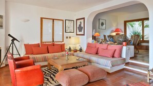 Uma sala de estar com sofá, poltronas, mesa de centro e um telescópio.
