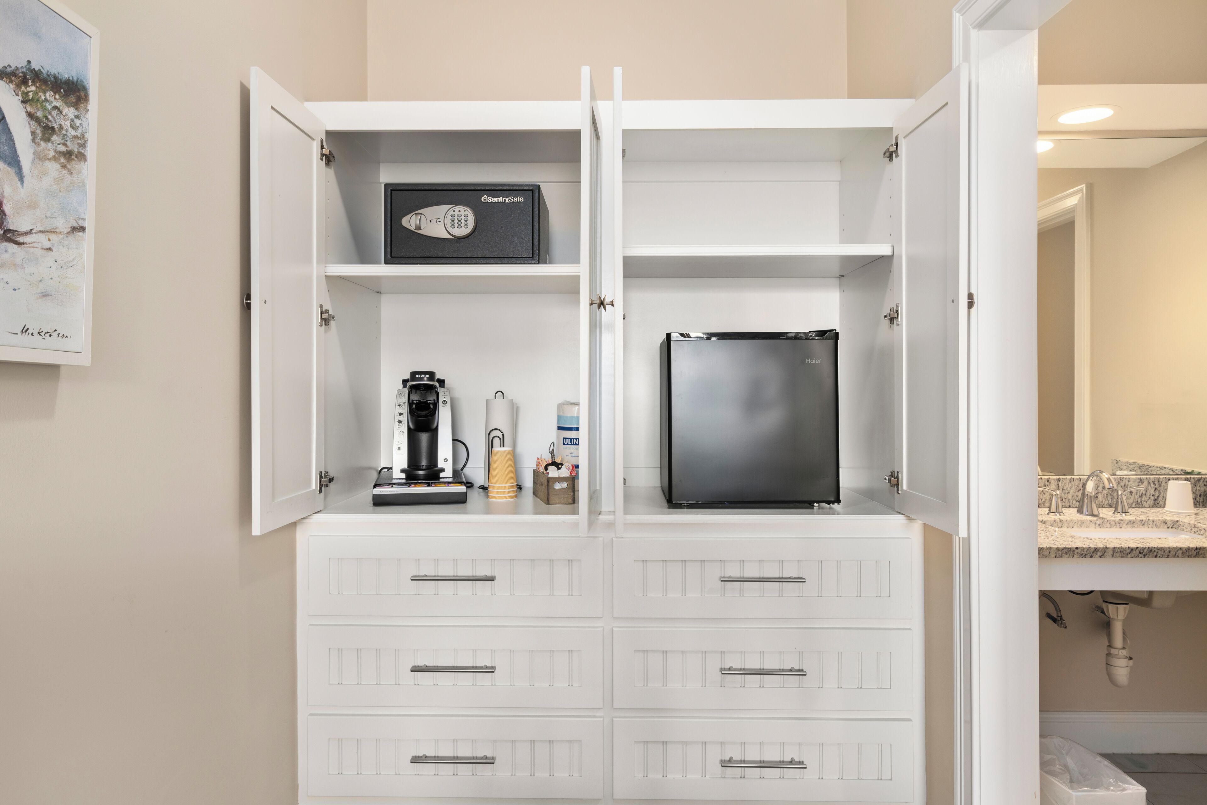 A compact minibar with a black refrigerator, a coffee maker, and a bottle of water.