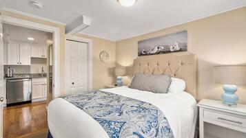 A bedroom with a large bed, a nightstand, a wall clock, and a painting of seagulls.