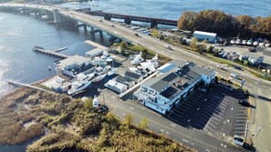 An aerial view of a marina with several boats docked, a bridge in the background, and a building with a large parking lot. - Guest House Suites (Salisbury)