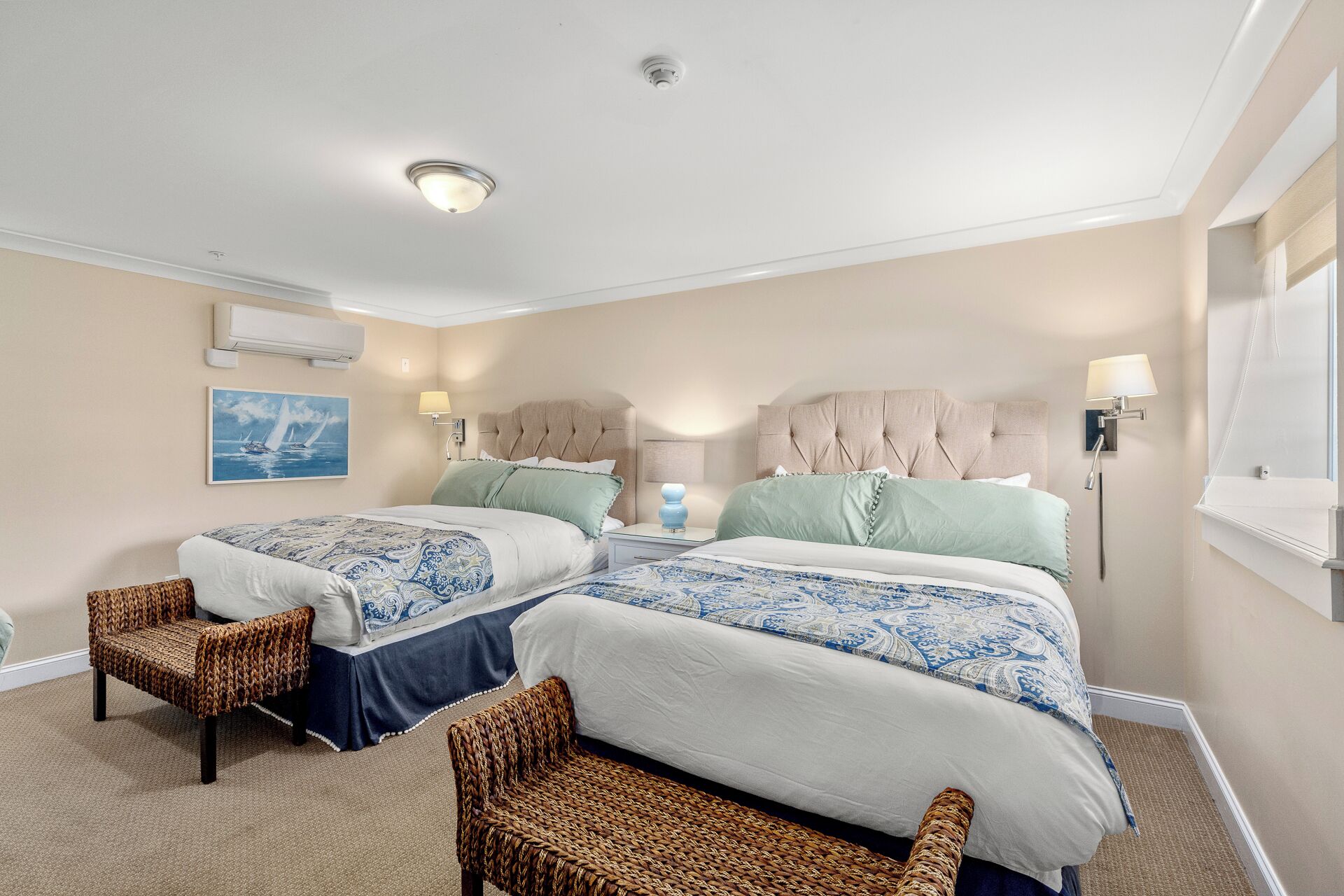 Una habitación de hotel con dos camas, sillones de mimbre, un cuadro y una ventana.