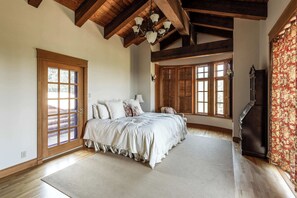 Ein Schlafzimmer mit einem großen Bett, Holzbalken, einer Kristallleuchtre und Blick ins Freie.
