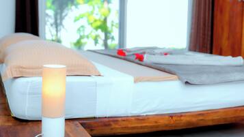 Una cama con colchón blanco, almohadas color beige y una mesita de noche con una lámpara blanca.