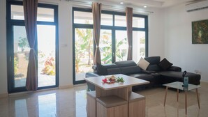 A modern living room with a sofa, a coffee table, and large windows with curtains. - EBENDE VILLA (Unguja South Region)