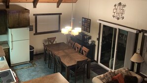 A cozy kitchen with wooden beams, a dining area with a table and chairs, and a living room with a sofa and a decorative wall sign.