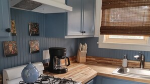 Una cocina con armarios azules, una estufa a gas, un horno blanco, una cafetera y una ventana con persianas.