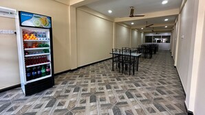 Un pasillo con una máquina expendedora llena de bebidas, una zona de descanso con mesas y sillas, y un suelo con diseño.