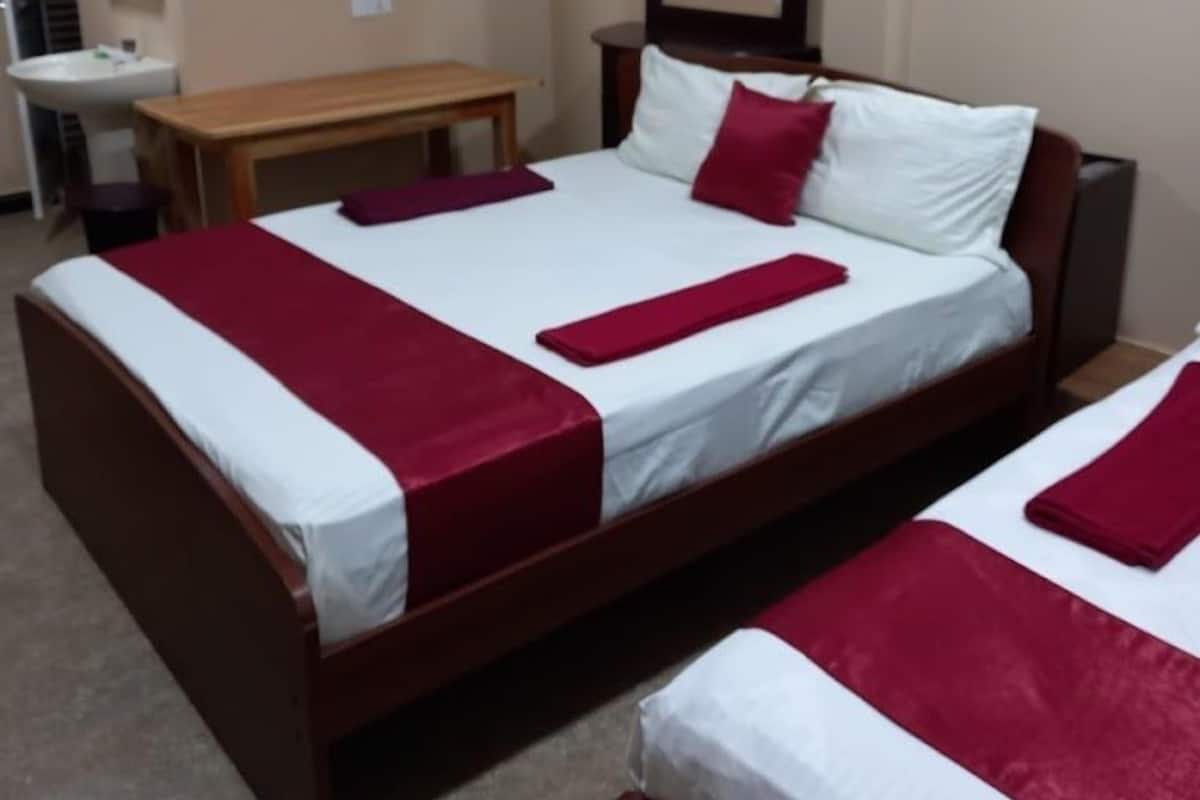 Habitación de hotel con dos camas, un banco de madera, un espejo y un lavamanos.