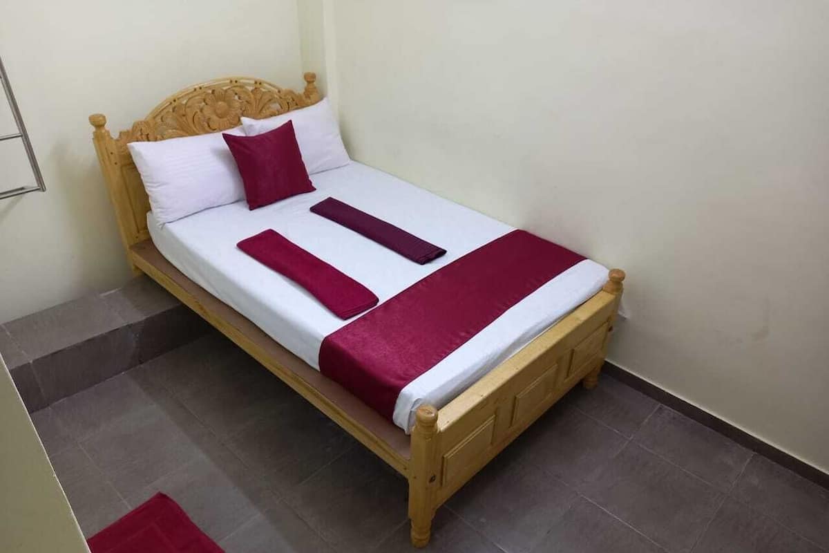 Una cama individual con cabecera de madera, ropa de cama blanca y granate, y una manta roja.