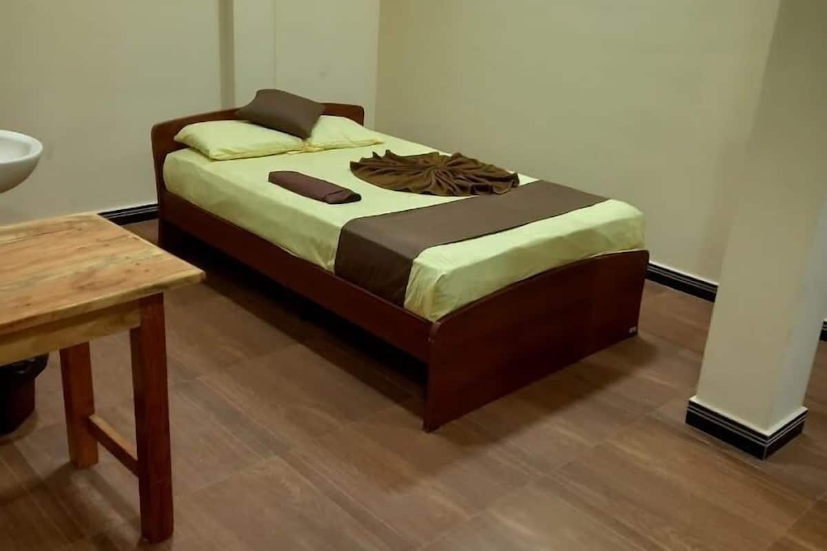 Una habitación pequeña con una cama individual, una mesa de madera y un lavamanos blanco.