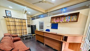 Una habitación con un sofá marrón largo, un escritorio de madera, una computadora y un estante de pared con pinturas religiosas.