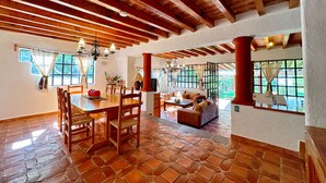 A spacious dining area with a wooden table and chairs, a cozy seating area with a sofa and armchairs, and large windows allowing natural light. - Sandunga Lago Tzintzuntzan (Tzintzuntzan)
