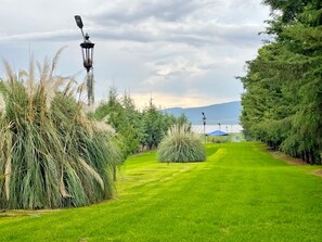 Un espace verdoyant bien entretenu, agrémenté d’un kiosque et de lampadaires, entouré d’arbres et de plantes de la famille des graminées.