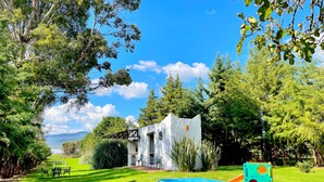 A grassy outdoor area with a white building, a blue play structure, and a white wall with a window. - Sandunga Lago Tzintzuntzan (Tzintzuntzan)