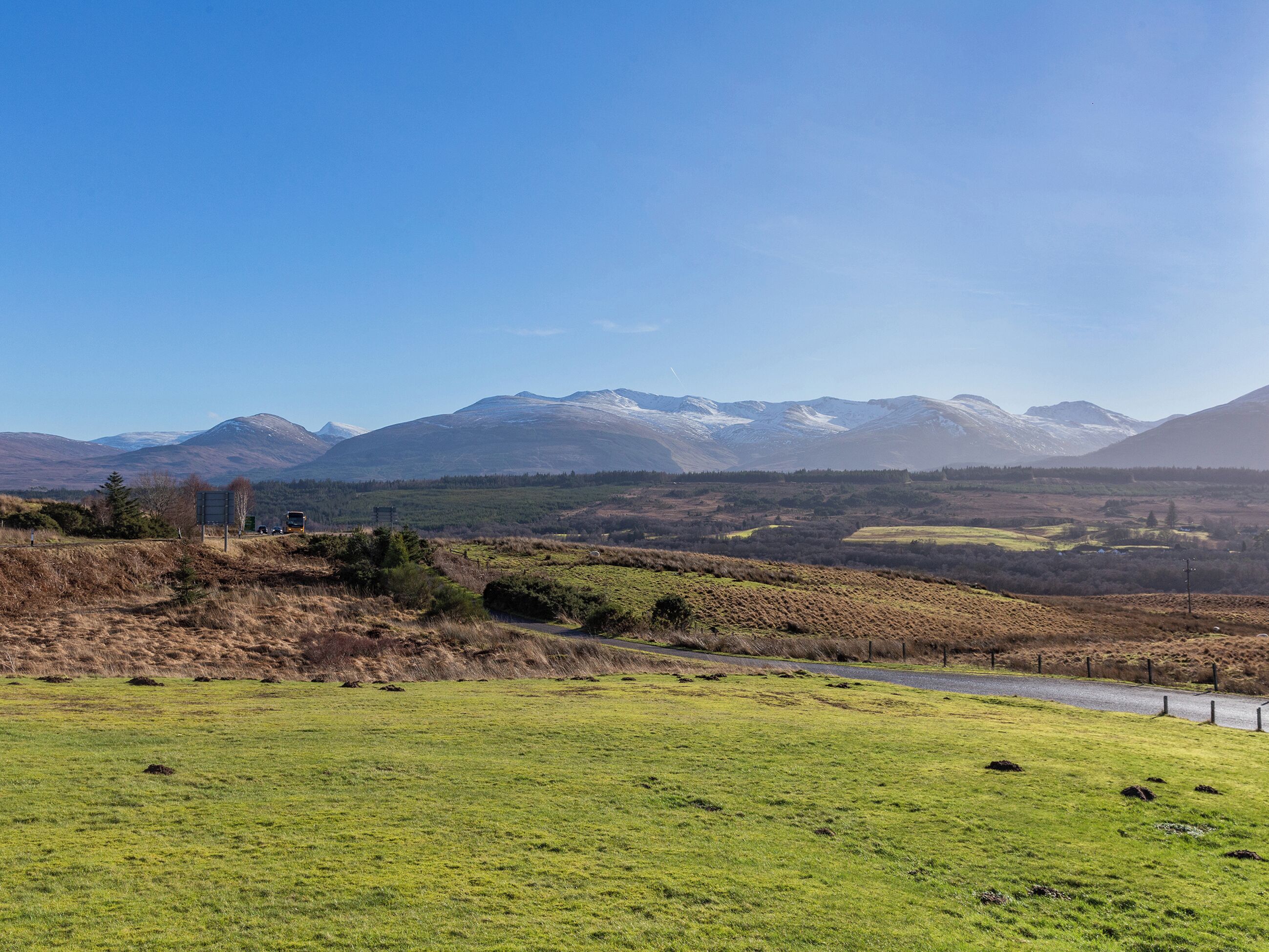 A rural landscape with a road, grassy fields, and distant mountains.