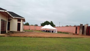 A building with a red door, a white tent in the background, and a grassy area in front.