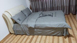 A bed with grey bedding and pillows featuring a prominent logo, a white headboard, and a wooden floor.