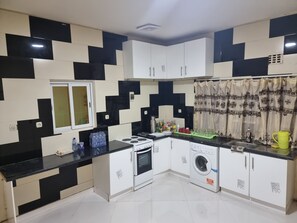 A kitchen with black and white checkered walls, a stove, oven, washing machine, and a window with a curtain. - Villa Sleeps 10 With Garden (Lubumbashi)