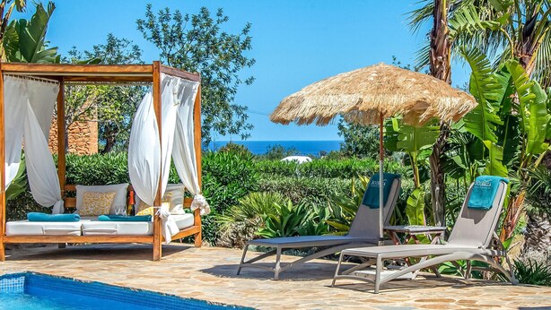Un espace aménagé au bord de la piscine, doté d’un auvent en bois, d’une chaise longue et d’un lit à baldaquin.