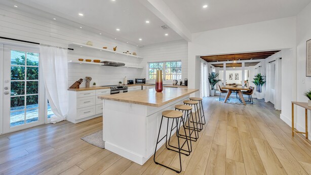 Een ruime keuken met een groot eiland, witte kasten en een eethoek met een houten tafel en stoelen.