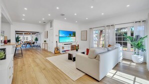 Een ruime woonkamer met een grote flatscreen televisie, een bank, een salontafel en een eethoek met een houten tafel en stoelen.