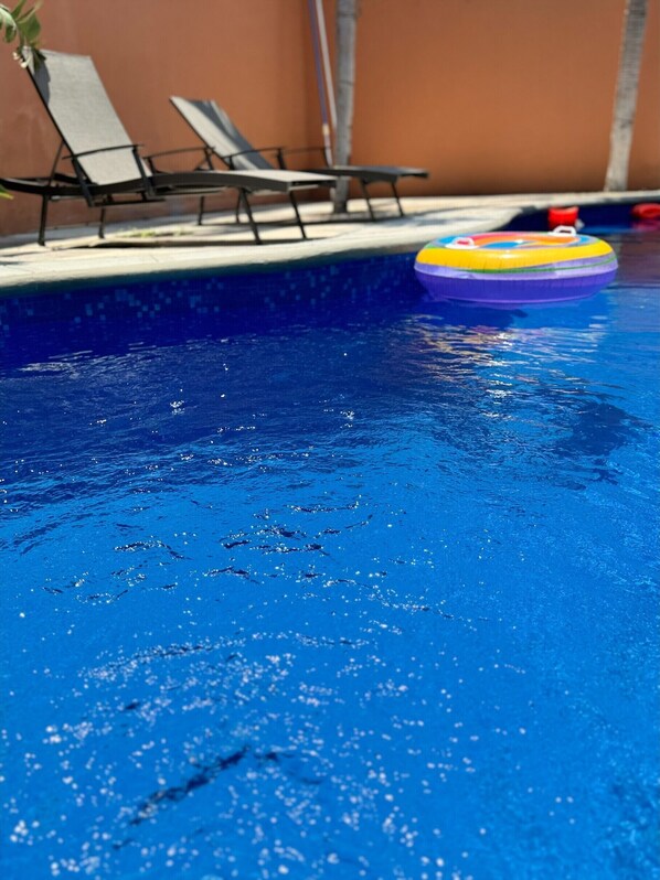 A swimming pool with clear water, lounge chairs, and a colorful inflatable ring.