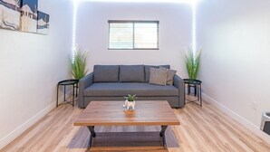 Een moderne woonkamer met een grijze bank, een houten salontafel en twee bijzettafels met planten.