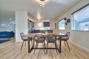 A modern kitchen with a wooden dining table and metal chairs, a blue sofa, and a large window with blinds. - Modern retreat with games room in central location! (Page)