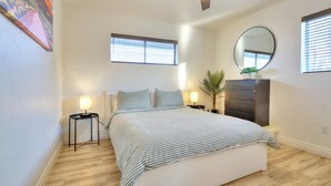 Een slaapkamer met een bed, twee nachtkastjes, een plafondventilator, een grote spiegel en een raam met zonwering.