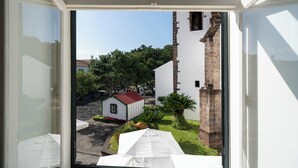 Blick aus einem Fenster auf einen Innenhof mit einem kleinen Gebäude, einer Backsteinstruktur und Grünflächen.