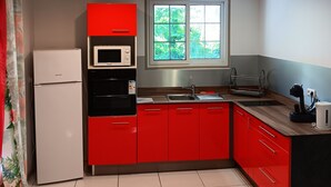 A modern kitchen with red cabinets, a white refrigerator, a microwave, and a sink.