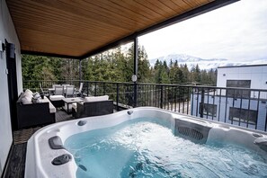 Un jacuzzi en una terraza cubierta con mobiliario exterior, con vista a un paisaje montañoso.