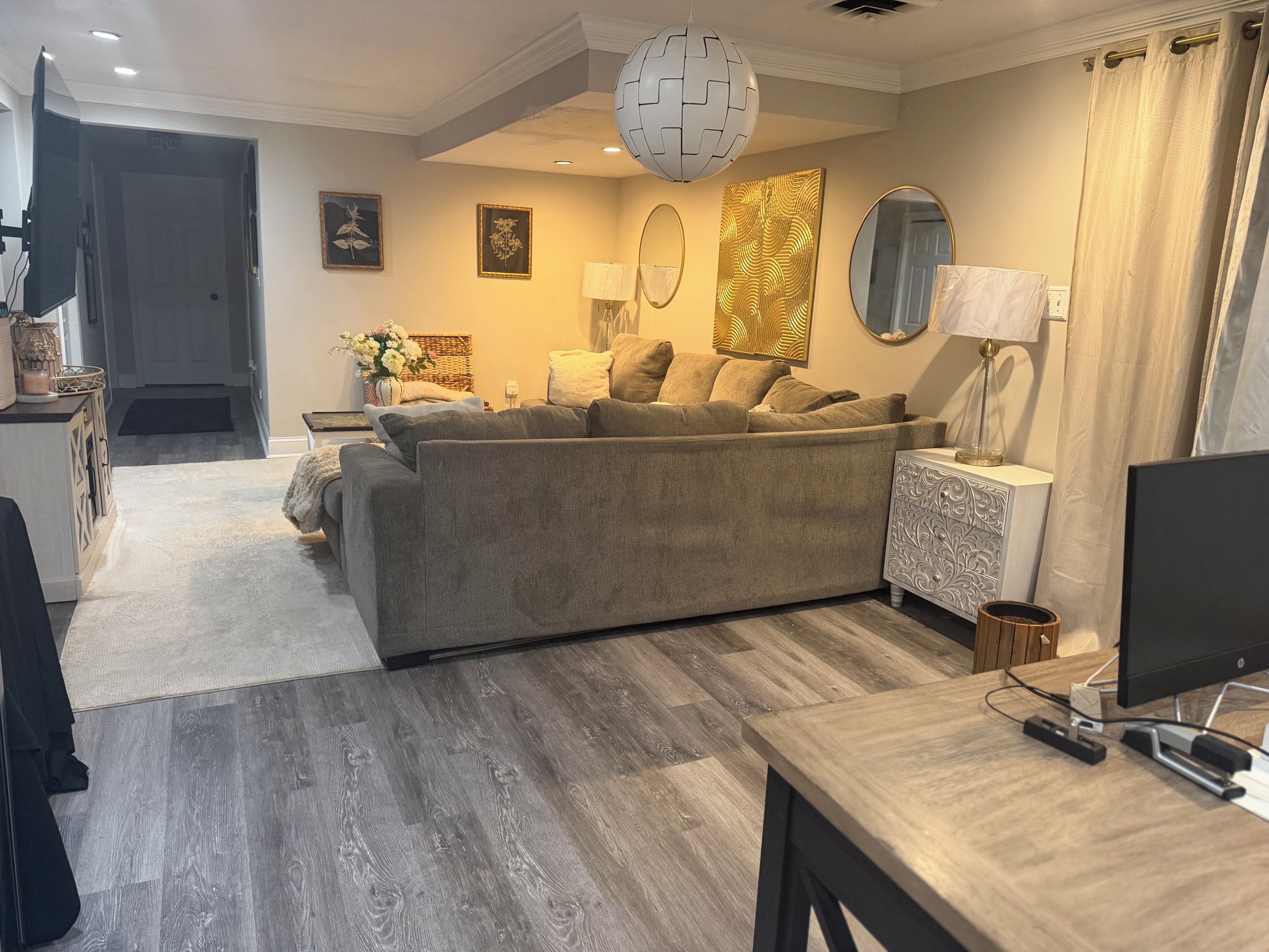 Een moderne woonkamer met een grijze bank, een houten salontafel, een televisie en een decoratieve spiegel.