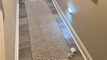 Un pasillo con un tapete estampado, una pared blanca y una puerta que da a un área de estar con un sofá y una mesa de centro.