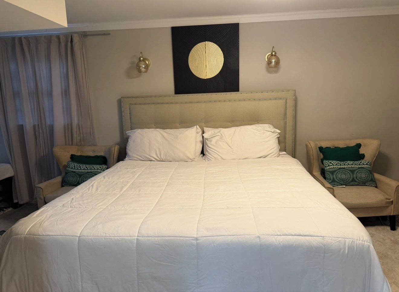 A hotel room with a large bed, two armchairs, a wall-mounted artwork, and a ceiling light fixture.