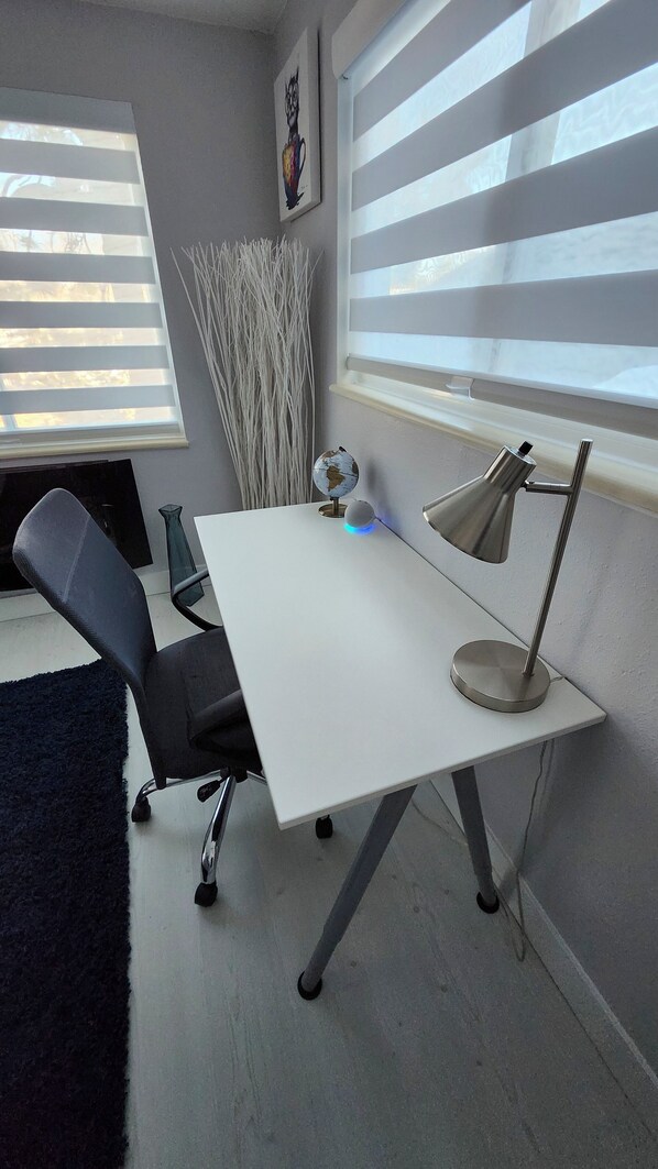 A modern office space with a white desk, a black office chair, a globe, a vase, and a lamp.
