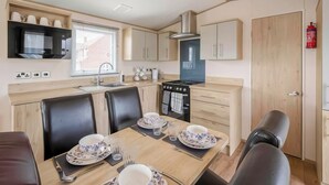 A compact kitchen with a microwave, stove, and sink. There are four chairs around a dining table set for four. - 2 bedroom accommodation in Retford (Retford)