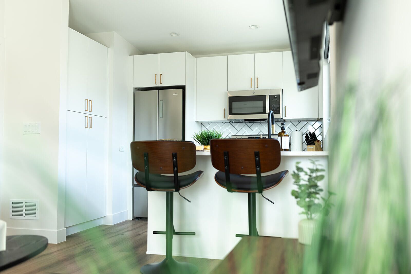 A modern kitchen with white cabinets, a microwave, and two bar stools with wooden seats.