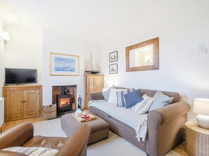 Ein gemütliches Wohnzimmer mit Sofa, Sessel, Holzschrank, Flachbildfernseher, Kamin und Wandbildern im maritimen Stil.