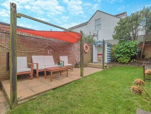 A patio with a wooden table, two white cushioned chairs, and a red canopy.