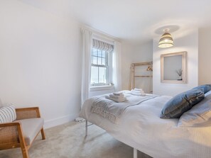 A bedroom with a bed, a chair, a window, a mirror, and a hanging light fixture.