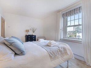 A neatly arranged bedroom with a bed, bedside table, lamp, and a view through a window.