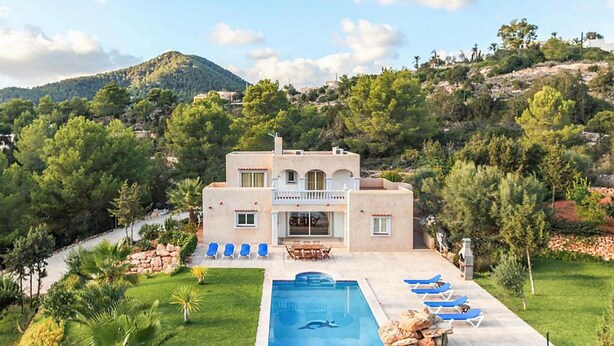Una villa de dos pisos con piscina, mobiliario exterior y vistas a las colinas circundantes.