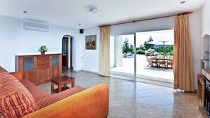 Amplia sala de estar con sofá, mueble de madera y comedor con asientos exteriores.