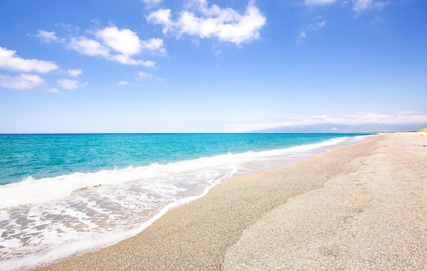A beach with clear turquoise water and a pebbly shore.