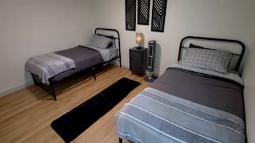 Un dormitorio con dos camas individuales, una mesita de noche con lámpara y una alfombra negra sobre piso de madera.